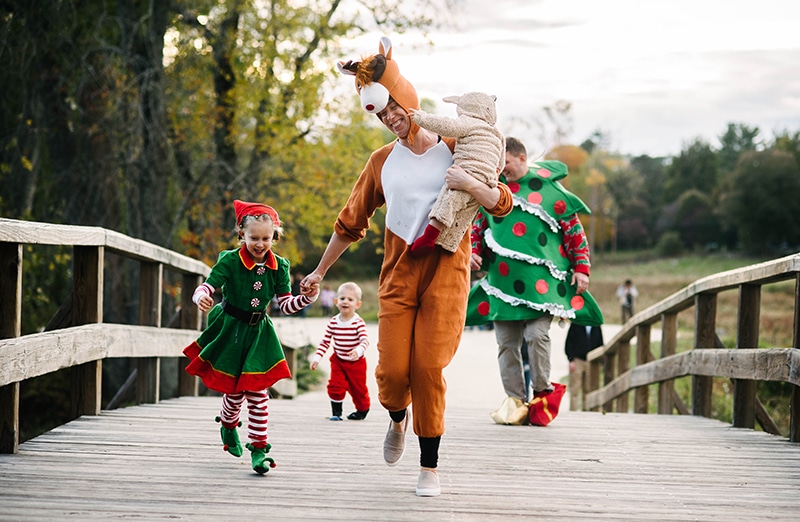a family of 5 dressed up in Christmas costumes excitedly runs across Concord's Old North Bridge