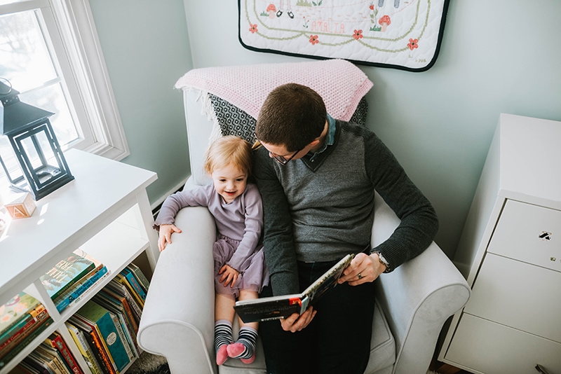 father reads to daughter in armchair