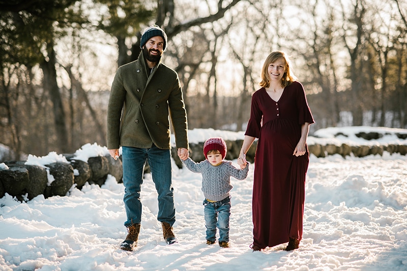 family of three holds hands in the snow during their family maternity session in Boston
