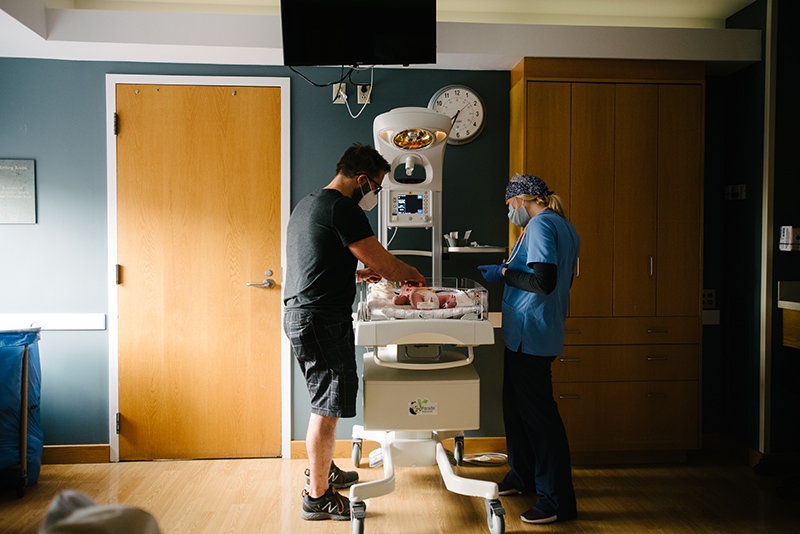 a new father looks on as the nurse examines his newborn son