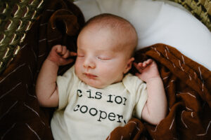 baby boy sleeps in a bassinet wearing a "C is for Cooper" onesie.