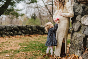 toddler girl places flower on her mom's baby bump during maternity photo session