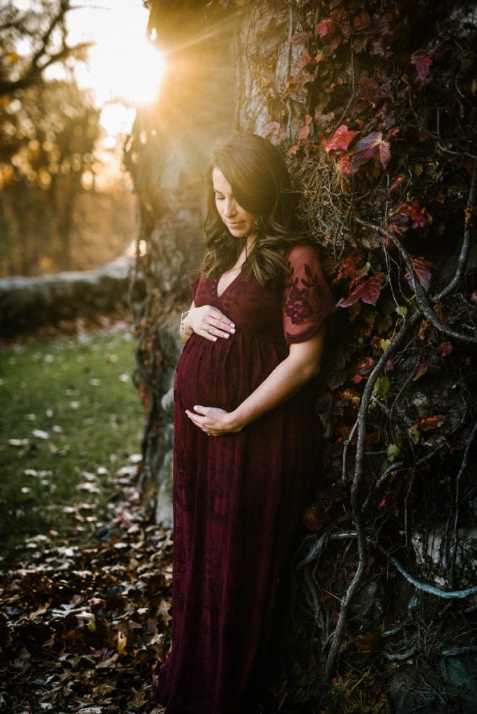 Newborn Photographer, a pregnant and expecting mother holds her belly wearing a dress outdoors during her maternity