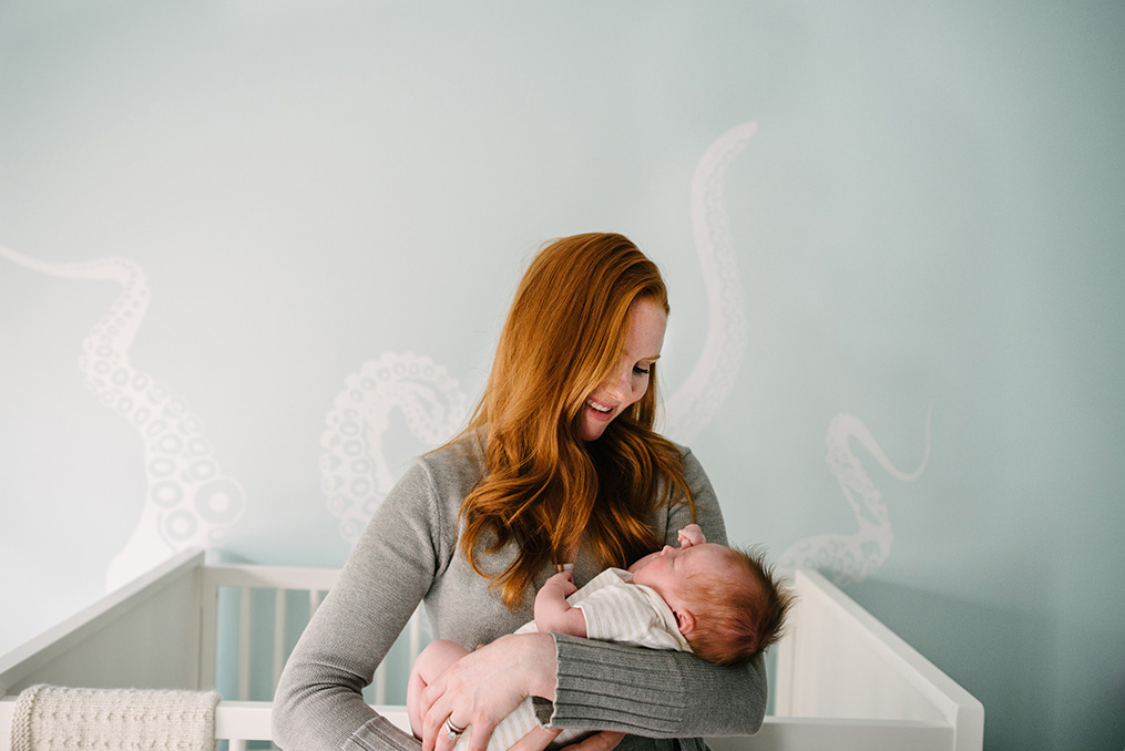 mom holds newborn girl in front of octopus accent wall during Somerville, MA newborn session