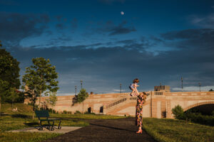 mother holds toddler daughter pup to the moon at dusk during their Harvard Square family session
