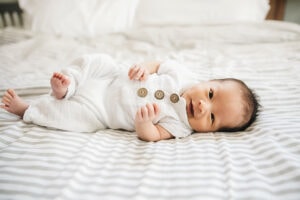 sweet newborn boy wearing a white romper with wooden buttons smiles during his newborn session