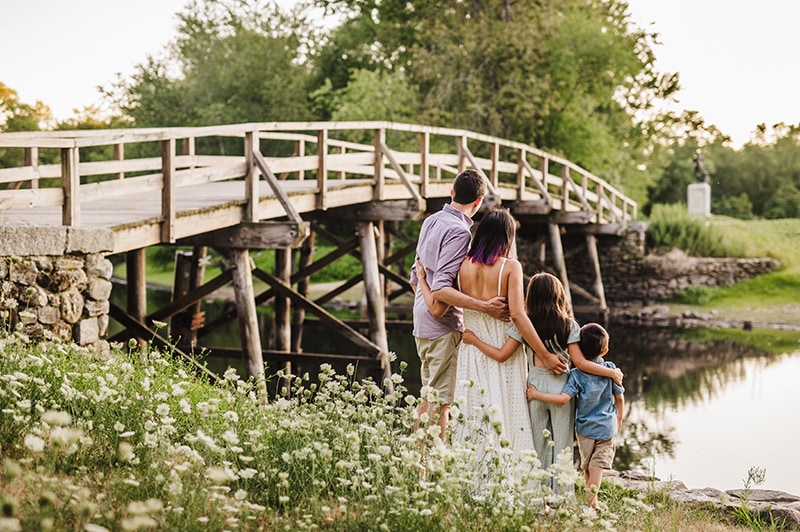 family stands embracing by Old North Bridge in Concord, MA