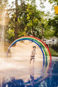 young boy runs through rainbow splash pad in Waltham