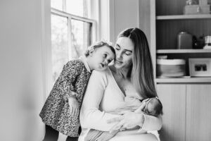 black and white image of mother nursing her newborn while toddler big sister snuggles up