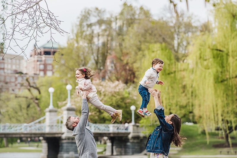 family of four throws their kids in the air in front of the bridge at Boston Public Garden