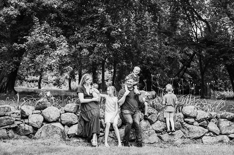 black and white image of family of 7 sitting on stone wall in Concord, MA